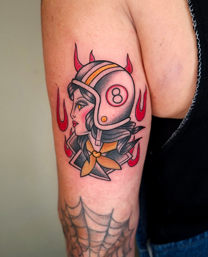 Tatouage old school représentant une tête de femme biker portant un casque de moto orné d’une boule de billard numéro 8.
