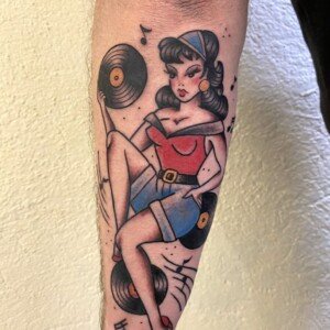 Tatouage pin-up oldschool avec vinyles et notes de musique sur le bras.