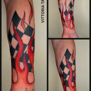 Tatouage racing old school avec flammes rouges et noires sur avant-bras, inspiration rally et départ de course, réalisé à Aubusson.