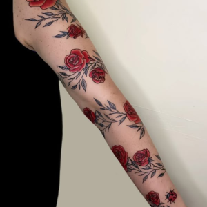 Tatouage floral représentant des roses rouges et feuillages le long du bras, réalisé à Aubusson par Vittoria Tattoo.