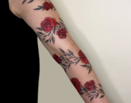 Tatouage floral représentant des roses rouges et feuillages le long du bras, réalisé à Aubusson par Vittoria Tattoo.