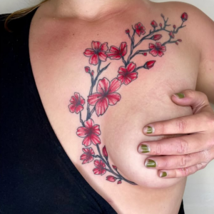 Tatouage floral rouge représentant une branche de fleurs de cerisier en finesse sur le décolleté, réalisé à Aubusson par Vittoria Tattoo.