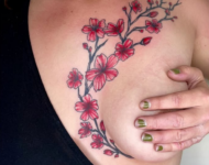 Tatouage floral rouge représentant une branche de fleurs de cerisier en finesse sur le décolleté, réalisé à Aubusson par Vittoria Tattoo.